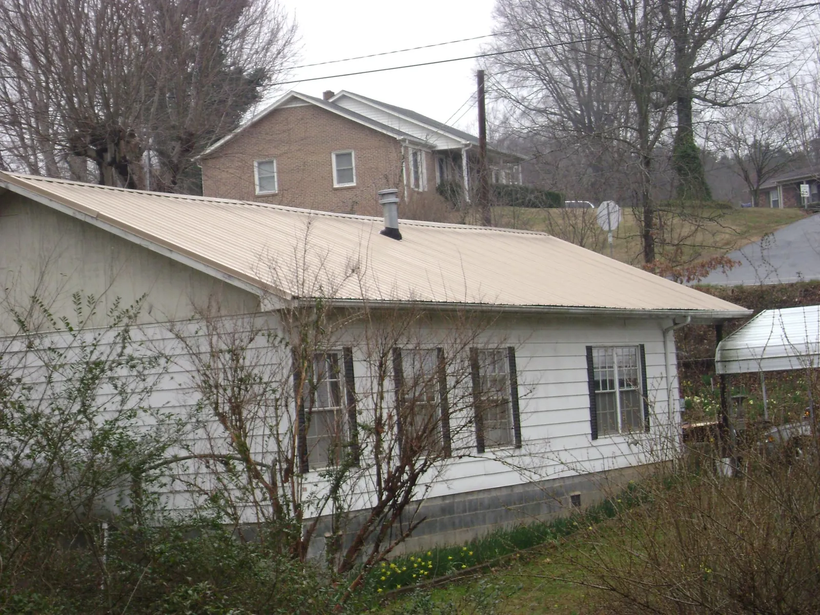Tan metal roof on a white sided house set into a hillside — Commercial Roofing by Roofing Brothers in Charleston